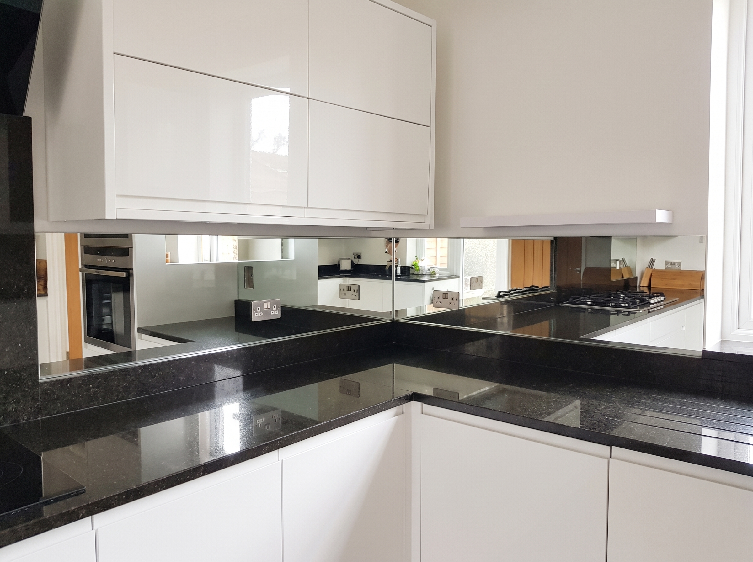 Silver mirror splashback with internal corner, fitted over a dark granite worktop